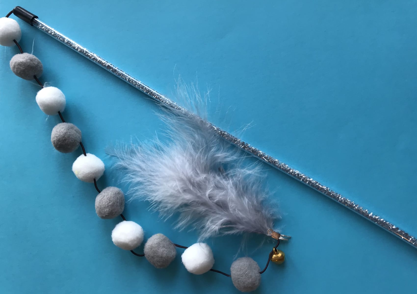 Grey and white pompom toy for your cat with fluffy balls and feathers on a stick